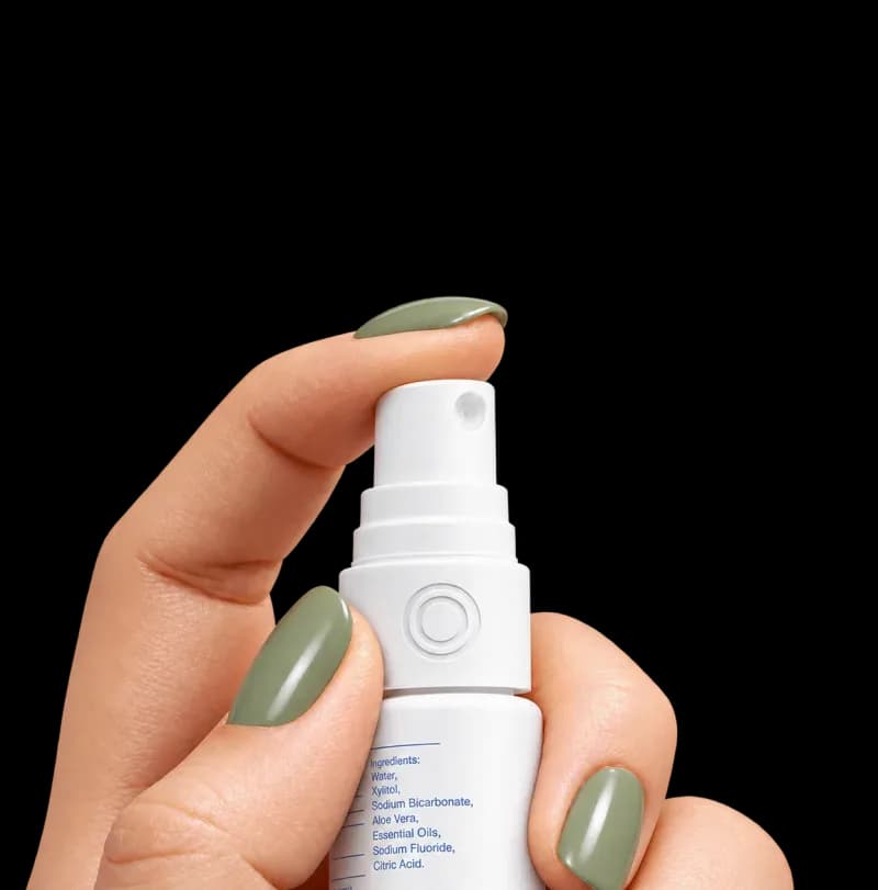 A hand with sage green nails holding a white oral spray bottle